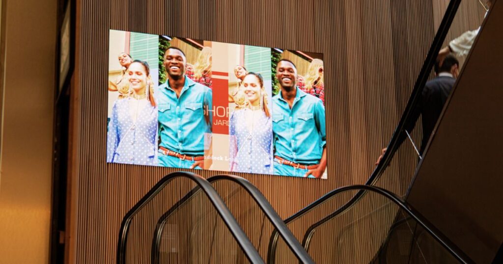 Painel de LED em parede de shopping center de luxo exibe imagem publicitaria de um casal usando roupas casuais 