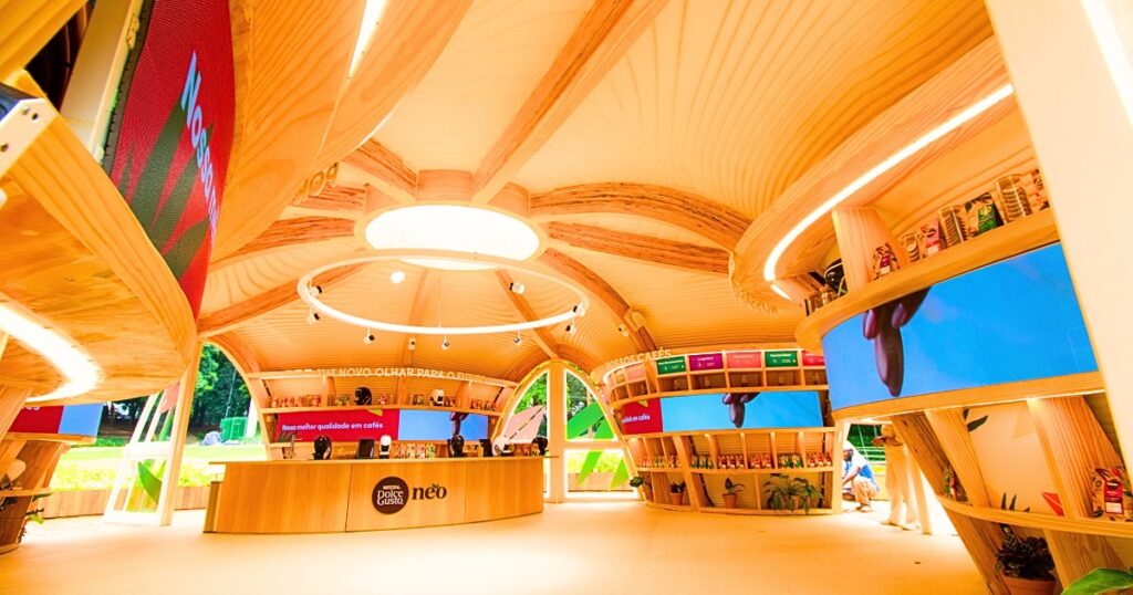 Imagem da loja conceito Dolce Gusto toda de material reciclado e sustentáveis. A arquitetura em formato cásulo de madeira clara e com painéis de LED curvos.